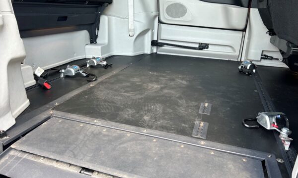 Empty van cargo area with metal tie-down anchors and track rails for securing cargo on a black rubber floor.