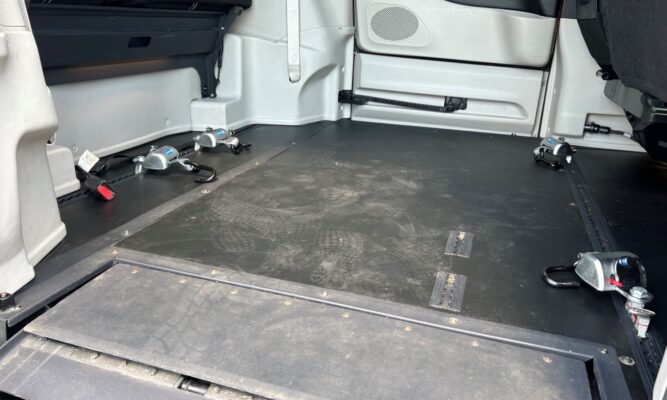 Empty van cargo area with metal tie-down anchors and track rails for securing cargo on a black rubber floor.