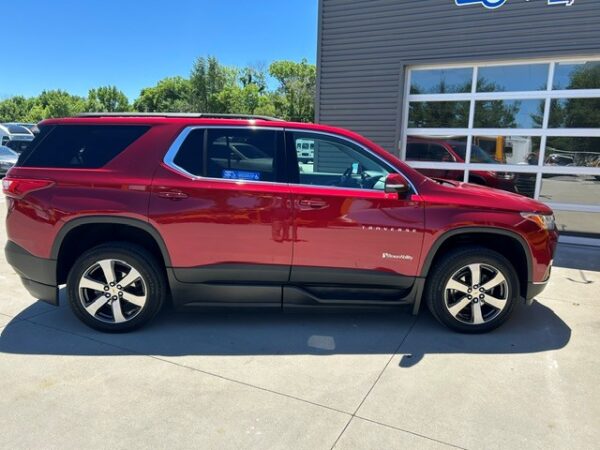 Side view of a red Chevrolet Traverse SUV parked at a dealership, showing black lower cladding and silver wheels.