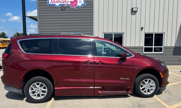 Maroon BraunAbility accessible minivan parked in front of a gray building with a Mobility sign overhead, showing a lowered side entry and sliding doors.