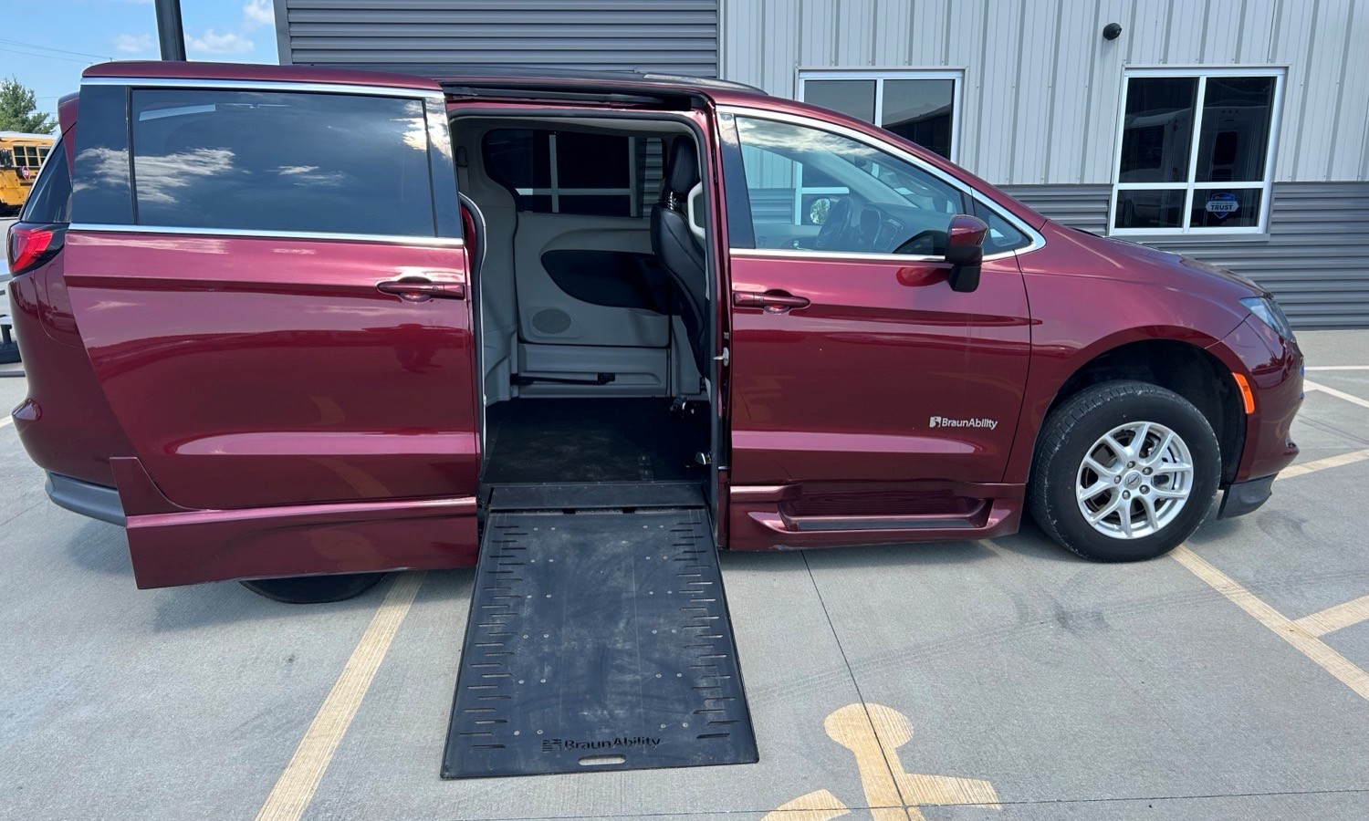 Maroon BraunAbility wheelchair-accessible van with ramp deployed and side door open in a parking lot.