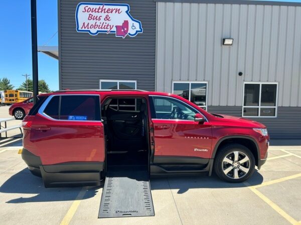 Red wheelchair-accessible minivan with ramp extended in a parking lot by a mobility services storefront.