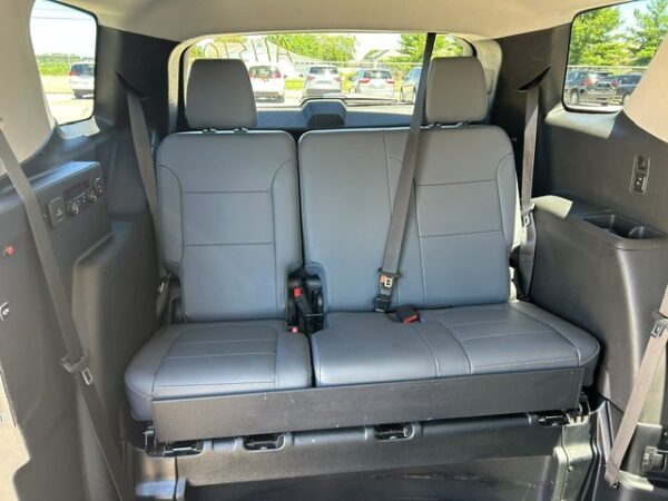 Inside a SUV, two gray leather captain's chairs in the second row with seat belts, view toward the rear; parked cars visible outside.