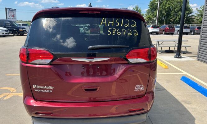 Rear view of a maroon BraunAbility Voyager minivan in a parking lot; yellow inventory numbers written on the rear window.