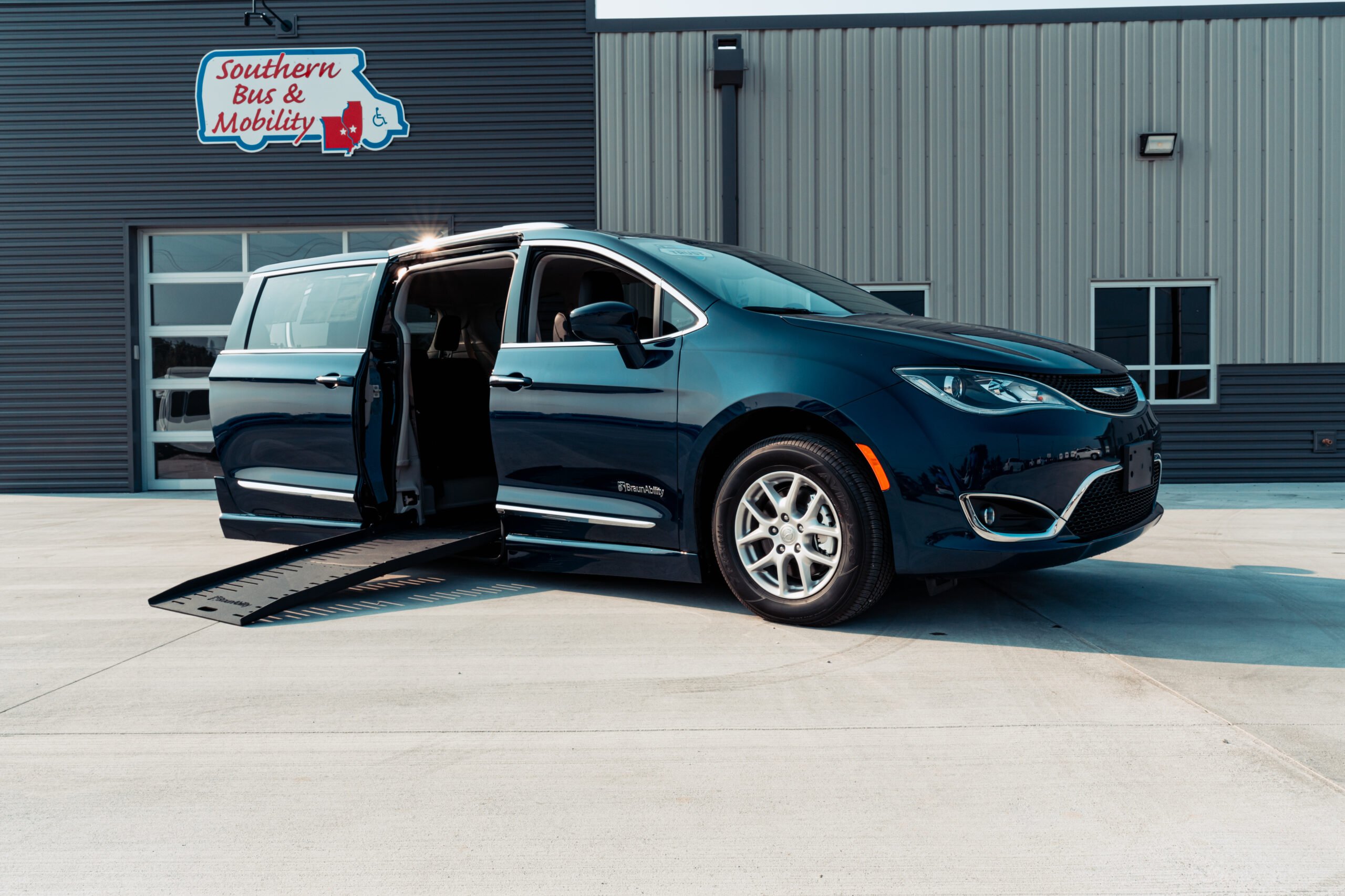 Blue wheelchair-accessible van with its side door open and an extended ramp at a mobility service facility.