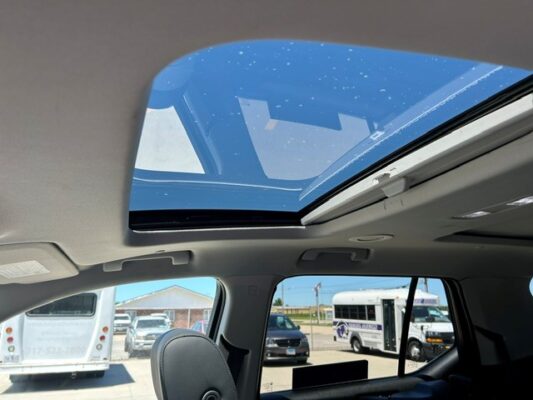 Interior of a car with the sunroof open, blue sky visible and buses parked outside.