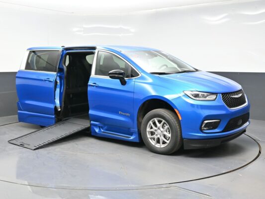 Blue wheelchair-accessible minivan with ramp extended and left-side door open, showing accessible entryway at the curbside position