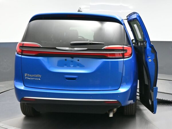 wav-2C4RC1BGXTR202255-5 Rear view of a blue BraunAbility Pacifica minivan with the right-side sliding door open, showing the cargo area, on a curved showroom floor.