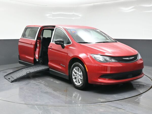 wav-2C4RC1CG9TR284610-0 Red handicap-accessible minivan with a lowered side ramp and the rear passenger door open in a showroom setting, ready for wheelchair access.