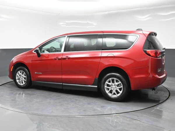 wav-2C4RC1CG9TR284610-3 Red minivan shown in a side profile in a studio setting, with rain droplets on the windows and body, alloy wheels visible.