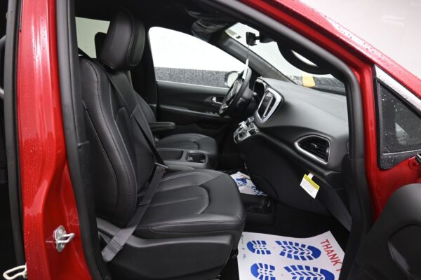 Front interior of a red car with black leather seats, steering wheel, and center console; driver-side door open.