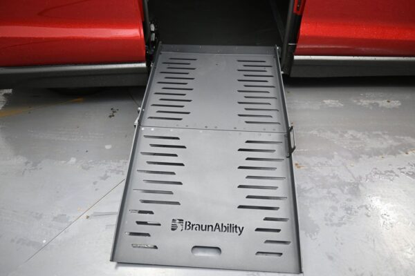 Wheelchair ramp extended from a red van, branded BraunAbility, down to a concrete floor.
