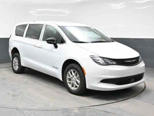 White mid-size minivan photographed indoors from a front-three-quarter view on a circular platform with tinted windows and chrome accents.