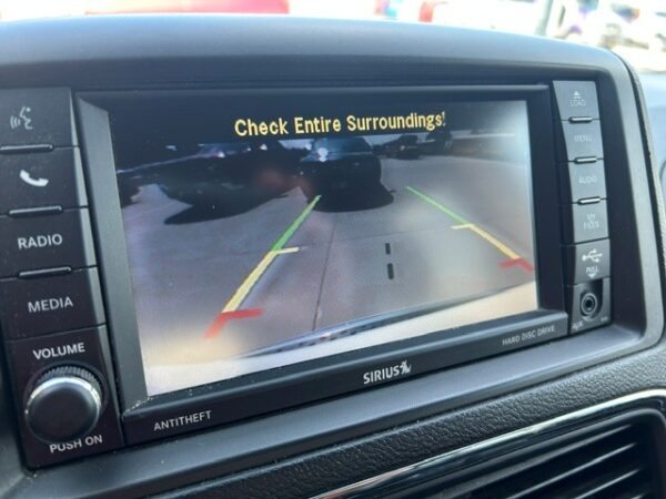 Rear-view camera display in a car dashboard showing parking guide lines (green, yellow, red) and the message 'Check Entire Surroundings!'