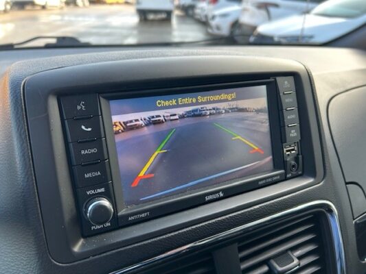 Car rearview camera display showing parking lot with green, yellow, and red guide lines and the warning 'Check Entire Surroundings!'