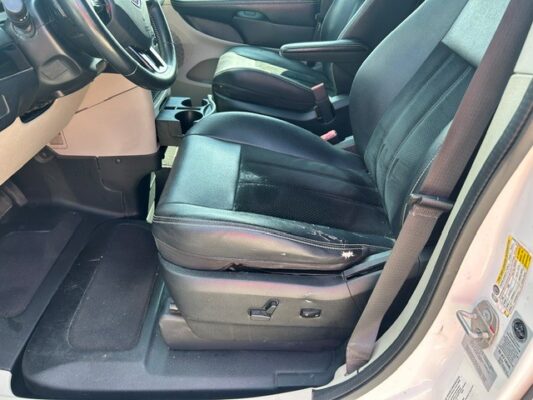 Interior of a vehicle showing the driver’s seat with black leather upholstery and noticeable wear on the seat edge; steering wheel and center console visible in the background.