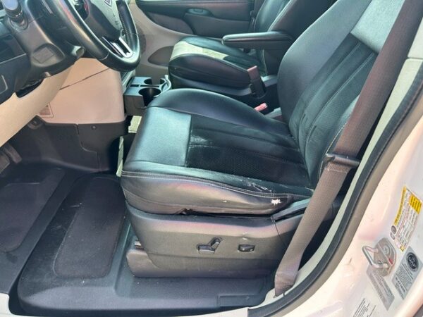 Interior of a vehicle showing the driver’s seat with black leather upholstery and noticeable wear on the seat edge; steering wheel and center console visible in the background.