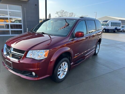 Maroon minivan parked on a dealership lot, front three-quarter view showing its chrome grille and clean exterior.