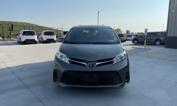 IMG_0387 Front view of a gray Toyota minivan facing the camera in a parking lot, with other cars and a building in the background.