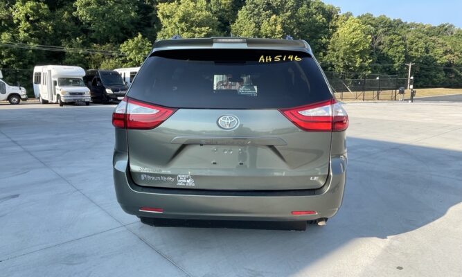 Rear view of a gray Toyota Sienna minivan parked in a lot, with a BraunAbility sticker on the lower left bumper and a yellow ID number on the rear window reading AH5146.
