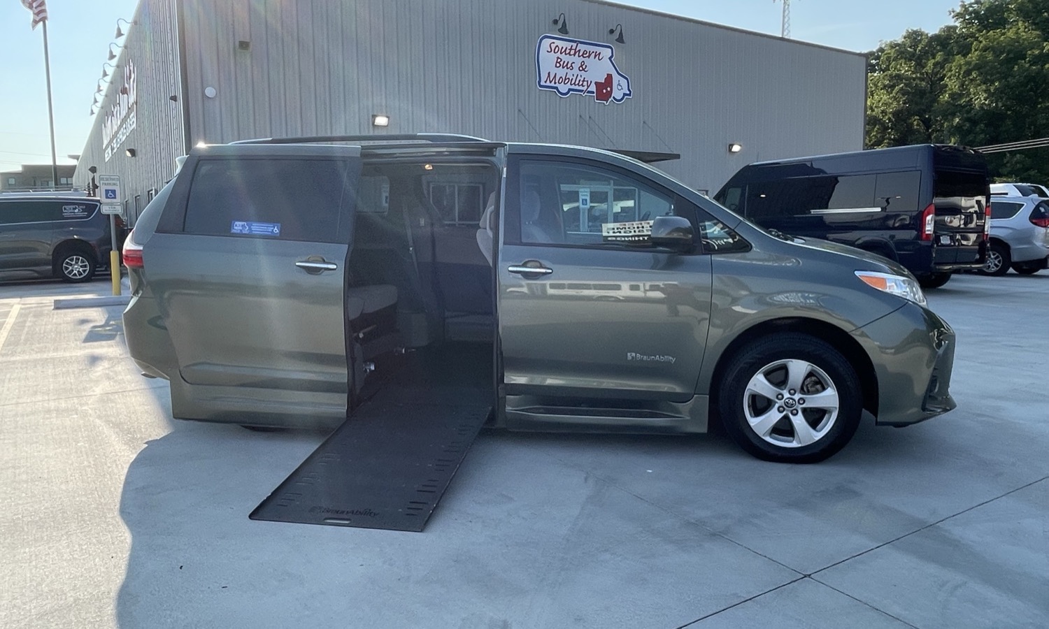 Gray wheelchair-accessible minivan with ramp extended from side door in a parking lot outside a mobility shop.
