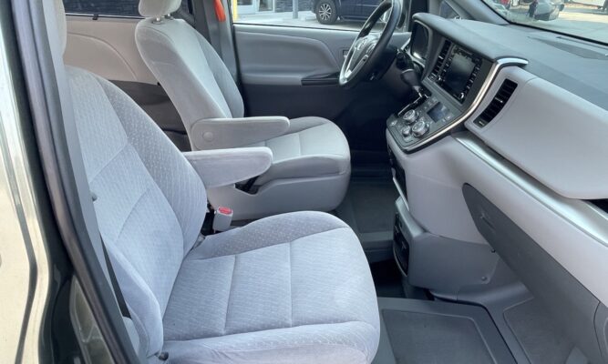 Interior of a clean van cockpit: driver and front passenger seats, gray fabric upholstery, and dashboard with center console visible
