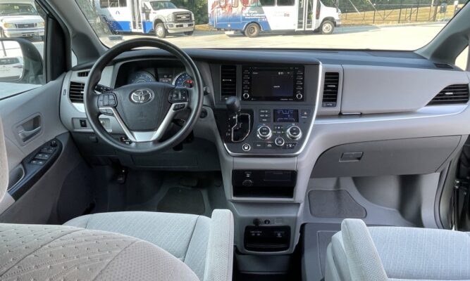 Interior of a modern minivan showing the steering wheel, center console with touchscreen, and front passenger seat.