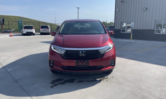 Front view of a red Honda SUV parked in a dealership lot with other cars and a building in the background.