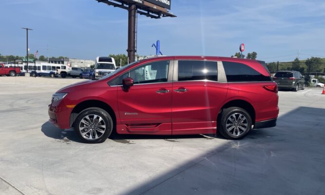 Red minivan (BraunAbility) parked in a lot, side view showing accessibility branding and lowered side step.
