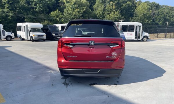 IMG_0441 Red Honda Odyssey seen from the rear in a parking lot with white buses in the background, BraunAbility badge visible on the right side of the tailgate.