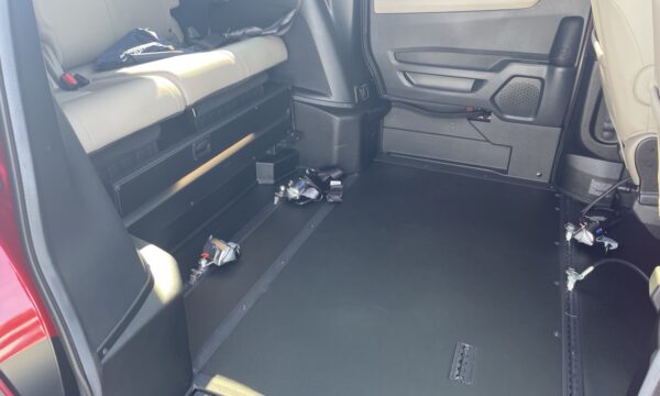 IMG_0444 Interior of a vehicle showing a flat cargo floor with folded back seats and scattered tools/clamps along the left side.