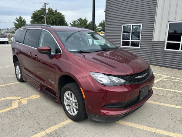 Maroon minivan parked in a parking lot beside a gray metal-clad building with windows, front visible.