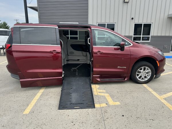 Maroon BraunAbility wheelchair-accessible van with ramp extended and side door open in a parking lot by a building district office complex.