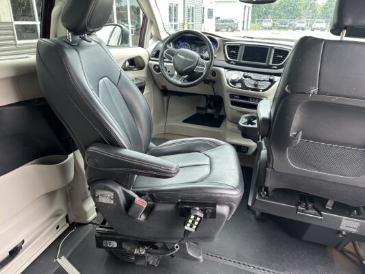 Interior of a modern minivan with leather driver seat, steering wheel, and dashboard; a floor-mounted wheelchair lift/mechanism visible near the pedals.