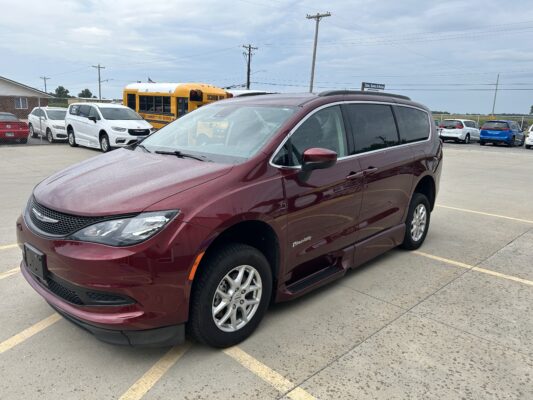 Maroon minivan in the foreground of a parking lot, with a yellow school bus and other cars in the background.