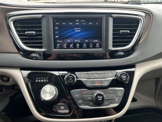 Infotainment touchscreen in a car showing FM radio 103.3 and surrounding controls, with air vents on either side and a gear selector below.