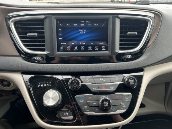 Infotainment touchscreen in a car showing FM radio 103.3 and surrounding controls, with air vents on either side and a gear selector below.