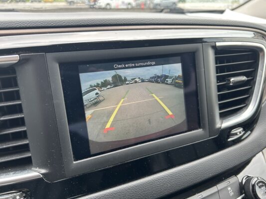 Rearview camera display on car dash showing a parking lot with yellow guide lines and the warning text 'Check entire surroundings'