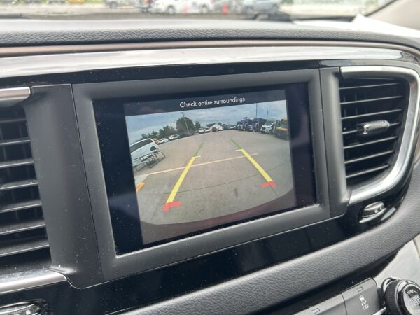 Rearview camera display on car dash showing a parking lot with yellow guide lines and the warning text 'Check entire surroundings'