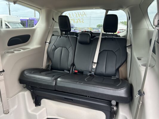 Rear row of black leather seats folded forward to create extra cargo space in a vehicle, shown from the rear interior with seatbelts visible and raindrops on the windows.