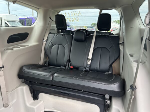Rear row of black leather seats folded forward to create extra cargo space in a vehicle, shown from the rear interior with seatbelts visible and raindrops on the windows.