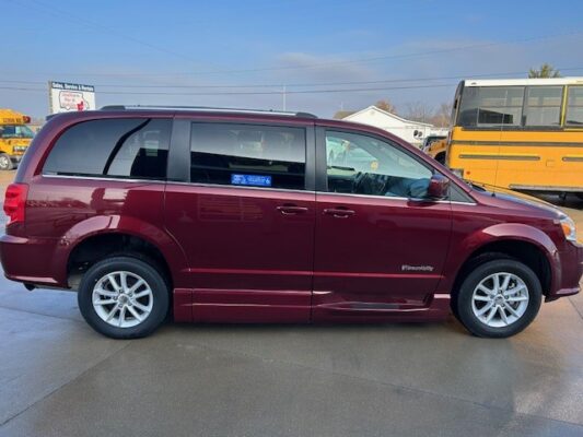 Maroon minivan seen in a parking lot, side profile with sliding door; a yellow school bus is in the background.