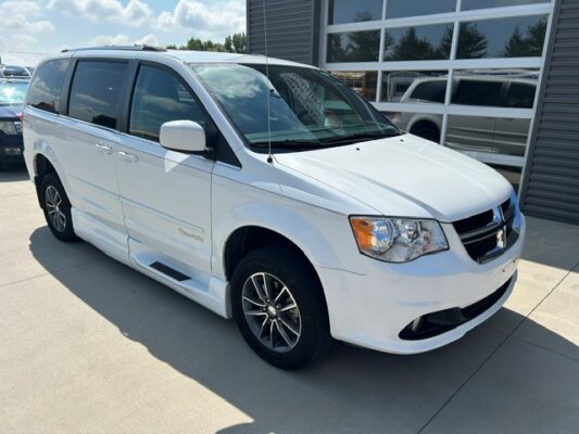 White minivan parked at a dealership, shown from the front three-quarter angle with chrome mirrors and alloy wheels.