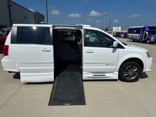 White wheelchair-accessible van with a lowered side-entry ramp; interior seating visible on a sunny dealership lot.
