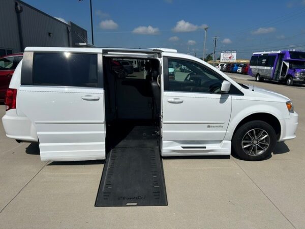 White wheelchair-accessible van with a lowered side-entry ramp; interior seating visible on a sunny dealership lot.