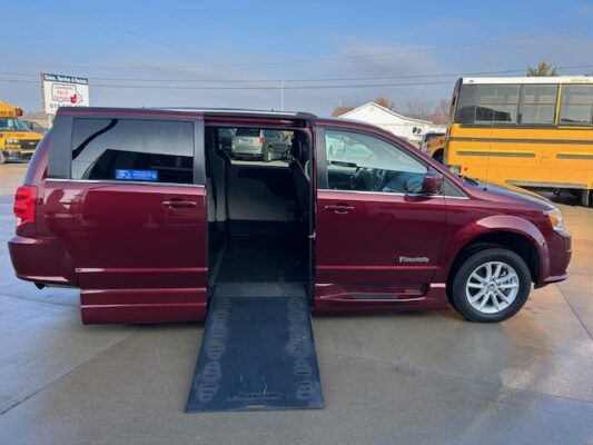 Maroon wheelchair-accessible minivan with a side ramp extended for wheelchair entry, parked in a lot.