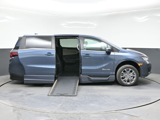 Blue minivan with a side-entry ramp extended to the floor, BraunAbility logo visible in a studio setting.
