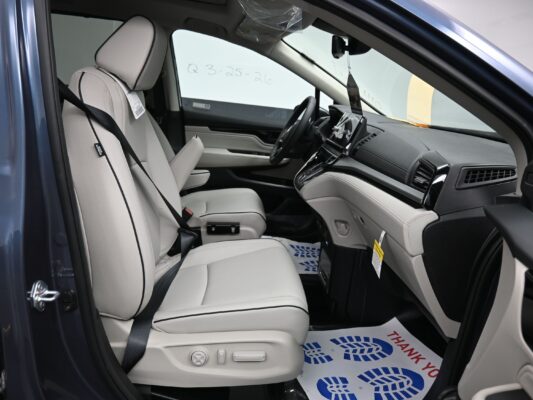 Interior of a new car showing light gray leather front seats, center console, and steering wheel from the passenger side door frame.