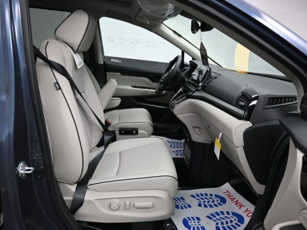 009 Interior of a new car showing light gray leather front seats, center console, and steering wheel from the passenger side door frame.