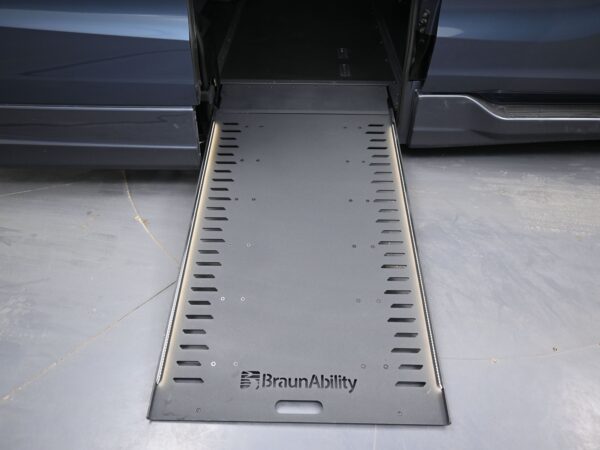 010 Wheelchair ramp deployed from a dark blue BraunAbility van, extending onto a gray floor with the BraunAbility logo visible on the ramp surface.